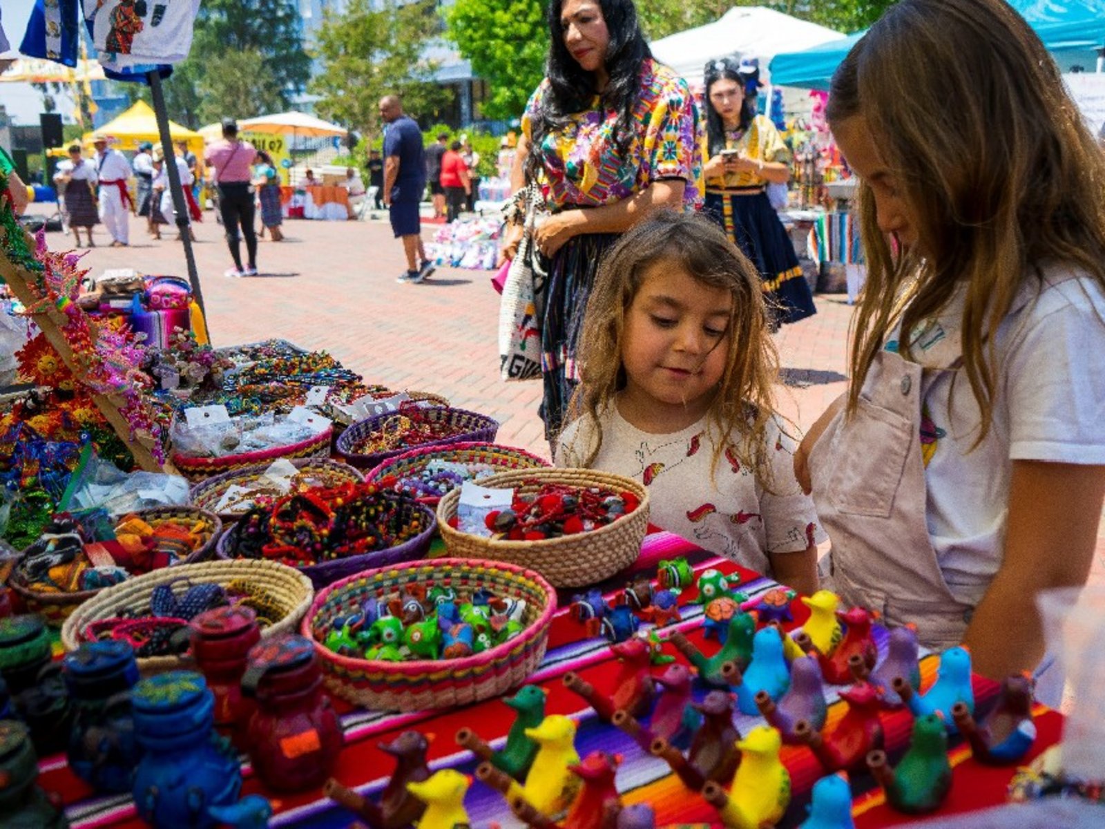Děti si vybírají z řady pestře malovaných dřevěných hraček a píšťalek ve stánku řemeslníků na mayském festivalu 9. července 2023 na L. Ron Hubbard Way
